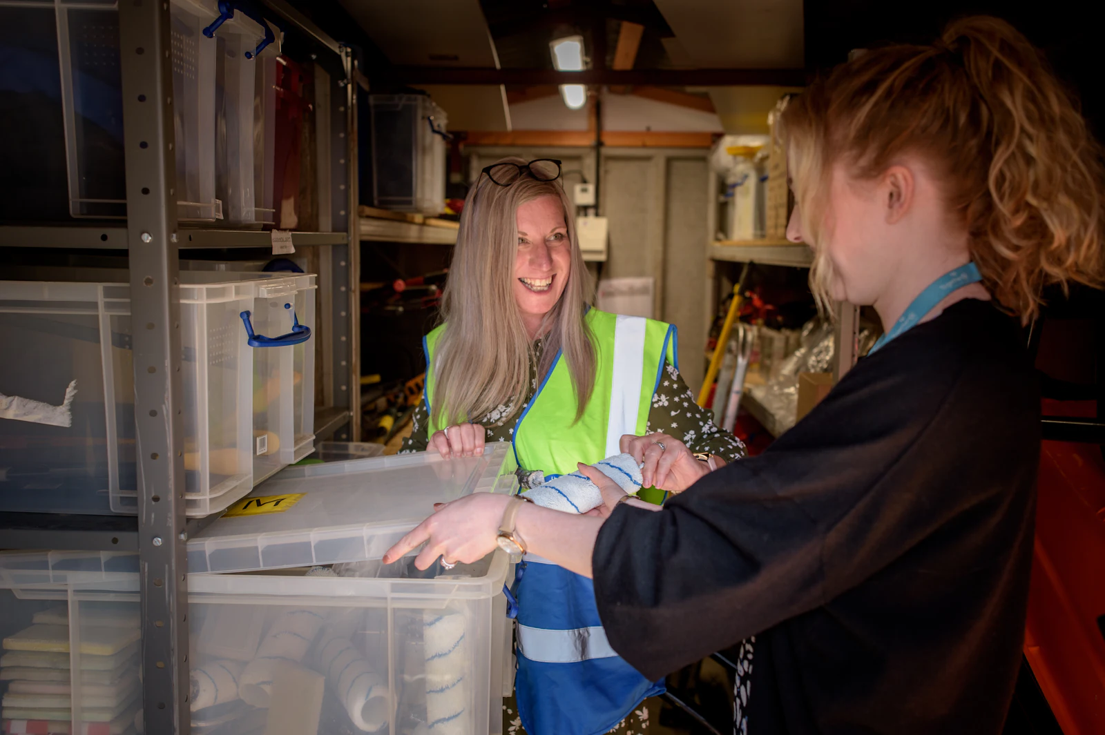 Two people checking stock together in a stockroom lined with shelves and bins